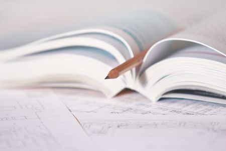 Architectural plan of house with open book and pencil. Close-up.