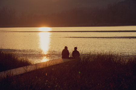Sunset on Lake Banyoles. We can see a couple of friends sitting contemplating the magical views.の写真素材