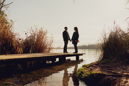 Young happy couple in a sea port on a lake. During the sunset. Holding hands and looking at each other.の写真素材