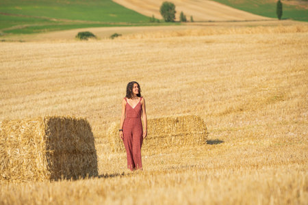 Pretty and smiling young girl with curly hair. Walking through a wheat field.の写真素材