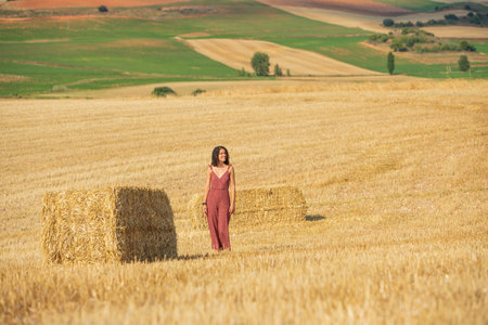 Pretty and smiling young girl with curly hair. Walking through a wheat field.の写真素材