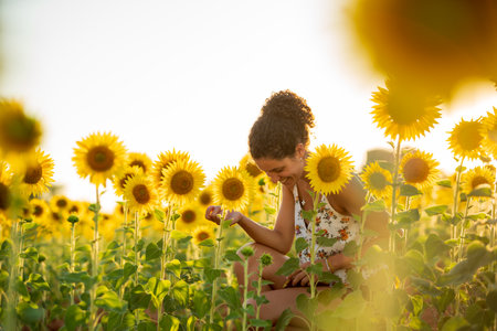 Young girl with curly hair in the middle of a field of sunflowers at dusk.の写真素材