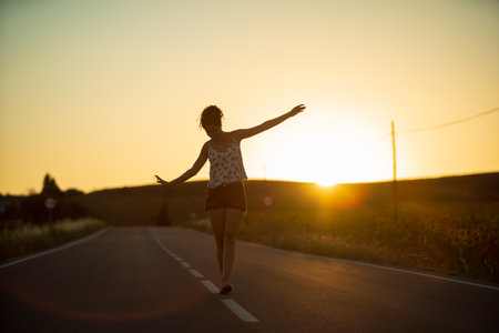 Young girl, walking in the middle of a lonely straight road, late in the day. With the hands stretched out in the shape of a cross, to maintain balance and not fall from the dividing line.の写真素材