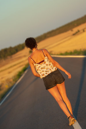 Young girl, walking in the middle of a lonely straight road, late in the day. With the hands stretched out in the shape of a cross, to maintain balance and not fall from the dividing line.の写真素材