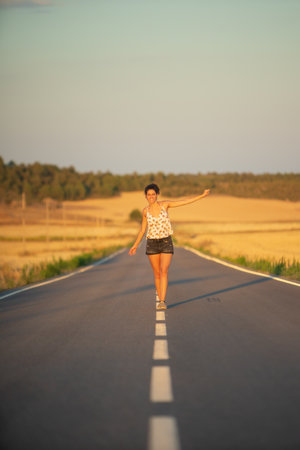 Young girl, walking in the middle of a lonely straight road, late in the day. With the hands stretched out in the shape of a cross, to maintain balance and not fall from the dividing line.の写真素材