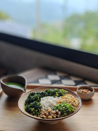 Hakka Thunder Tea Rice (Lui Cha) , 45-degree angle shot with forest window view. Rice with kale and chickpeas in bowl on wooden tableの写真素材