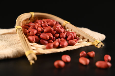 Red peanuts in a bamboo sieve on a black background closeupの写真素材