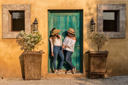Two girls with beige hats posing in front of a green door on a sunny afternoonの写真素材