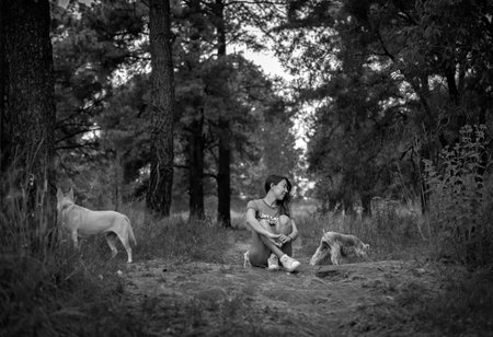 Latin girl playing with her dogs in the woods sitting on floor having a great timeの写真素材