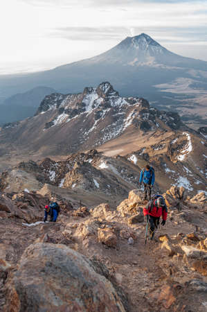 Sunrise at the top of the mountain with some mountaineers climbing up and a volcano in the...