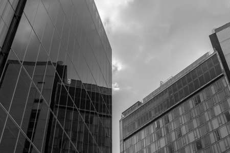 Partial view from below of two office buildings with a some clouds in the sky in black and white....