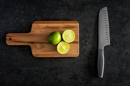 Flat lay of fresh limes on cutting board with knife on black stone background. Top view with copy space.の写真素材