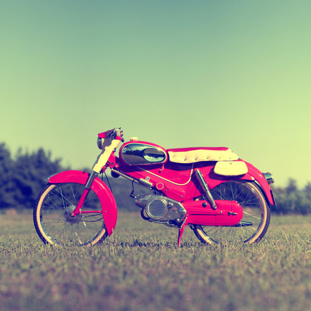 Retro motorcycle concept. Red vintage bike in field. Retro style photo with noise, square crop and copy space.の写真素材