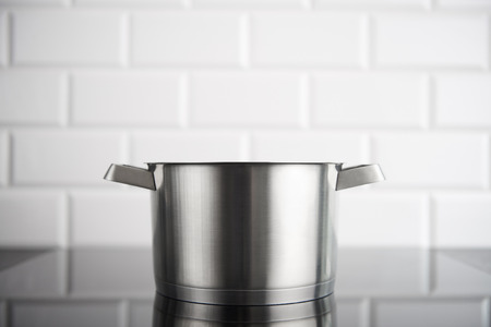 Stainless steel pot without cover on the induction stove with white metro tiles in the background. Copy space.の写真素材