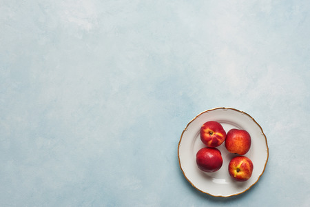 Flat lay of fresh nectarines fruits on white rustic plate on light blue background. Top view with copy space.の写真素材