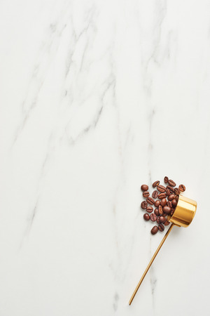 Concept of coffee background. Flat lay of golden scoop with coffee beans on marble background. Top view with copy space.の写真素材