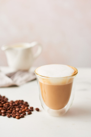 Cappuccino in a double walled glass with roasted coffee beans. Feminine rose background with copy space. High resolution image, narrow depth of field.の写真素材