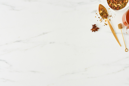 Flat lay of fresh black tea, with golden spoon, dipper and herbs on white marble background. Top view with copy space.の写真素材
