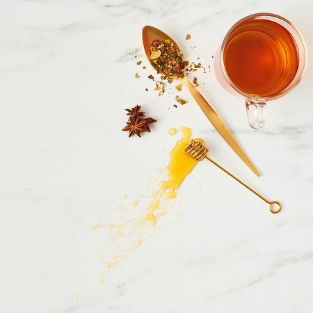 Tea concept. Top view of fresh black tea, with golden spoon, dipper with honey and herbs on white marble background. Flat lay, square crop.の写真素材