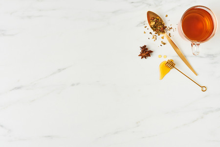 Tea concept. Top view of fresh black tea, with golden spoon, dipper with honey and herbs on white marble background. Flat lay with copy space.の写真素材