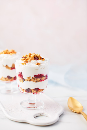 Healthy raspberry yogurt parfait in a glass with golden spoon on white marble table over pink background with copy space.の写真素材
