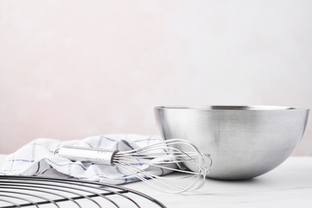 Baking concept. Bowl with a whisk, dishcloth and French wire rack on white marble table over pink background with copy space.の写真素材