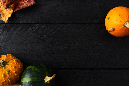 Simple autumn background with yellow leaf, green and orange pumpkins on black wood with copy space. Top view.の写真素材