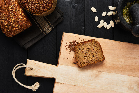 Cutting board with slice of bread, linseed and various crusty whole wheat bread, pumpkin seeds and...
