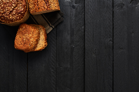 Various crusty whole wheat bread and slices of bread on black wooden table. Top view with copy space for text, menu or recipes.の写真素材