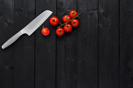 Stainless steel vegetable knife and tomato on black wooden table with copy space for menu or...