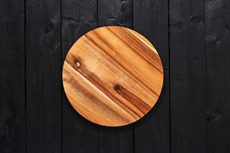 Top view of round wooden serving plate on black wooden table with copy space.の写真素材