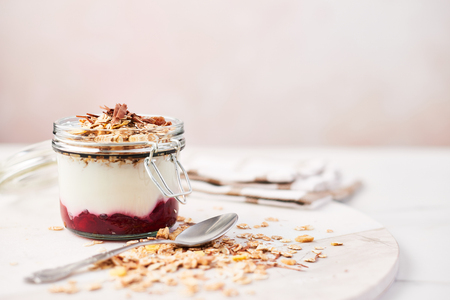 Healthy breakfast. Jar of healthy yogurt with strawberry sauce, oat and chocolate on white marble serving plate over pink background with copy space.の写真素材