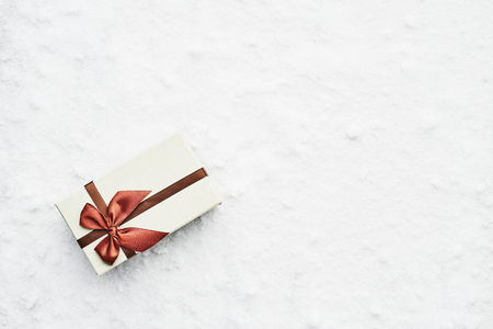 Top view of wrapped Christmas gift box with maroon ribbon on the snow. Copy space for text.の写真素材