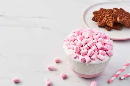 Hot chocolate or cocoa with whipped cream and pink marshmallow candy in pink and white mug with Christmas gingerbread cookie on white marble table. Copy space for text.の写真素材