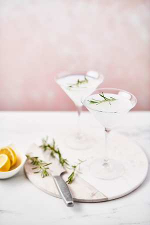 Summer drink. Refreshing summer alcoholic cocktail Margarita with rosemary and citrus fruits or sparkling gin and lemonade on white marble table over pink background. Copy space. Selective focus.の写真素材