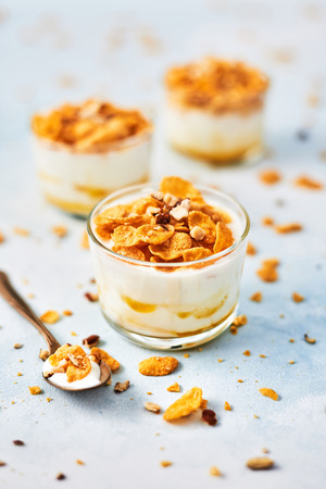Healthy breakfast or dessert. Tasty corn flakes with yogurt, almond and honey in a small glass on light blue background. Copy space for text.の写真素材