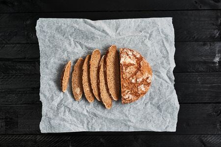 Sliced bread on baking paper over black wooden background. Delicious freshly baked bread. Top view....