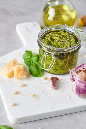 Pesto sauce or pesto genovese in a glass jar with pine nuts, parmesan, basil, oil and garlic on white marble cutting board. Copy space.の写真素材