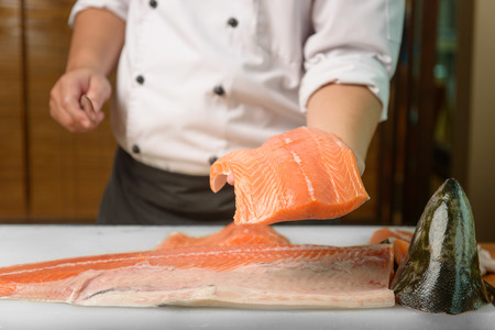 Chef preparing a fresh salmon on a cutting board, Japanese chef in restaurant slicing raw fish for salmon sushi, ingredient for seafood dish.の写真素材