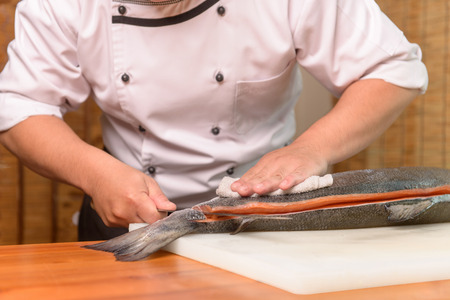 Chef preparing a fresh salmon on a cutting board, Japanese chef in restaurant slicing raw fish for salmon sushi, ingredient for seafood dish.の写真素材