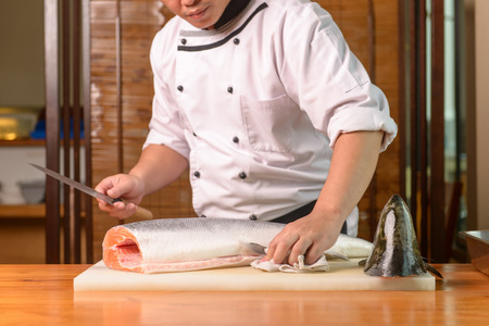 Chef preparing a fresh salmon on a cutting board, Japanese chef in restaurant slicing raw fish for salmon sushi, ingredient for seafood dish.の写真素材