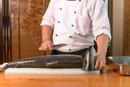 Chef preparing a fresh salmon on a cutting board, Japanese chef in restaurant slicing raw fish for salmon sushi, ingredient for seafood dish.の写真素材