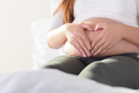 Pregnant Woman holding her hands in a heart shape on her baby bump. Pregnant Belly with fingers Heart symbol.の写真素材