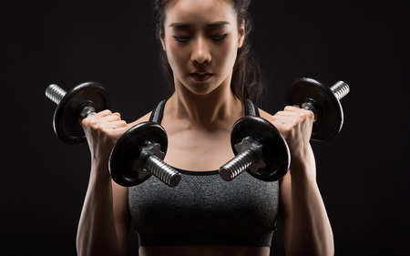Beautiful girl exercising squatting with dumbbells on black.の写真素材