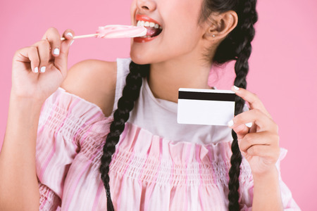 portrait of happy young girl showing credit card  with candy over pink background,easy Business...