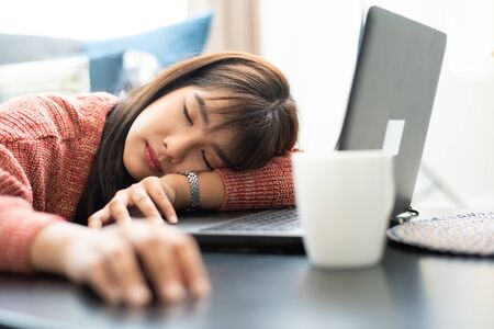 Tired businesswoman sleeping on table in office. Young Asian woman working from home. Woman using laptop. Entrepreneur, business, freelance work, student, stress, work from home conceptの写真素材