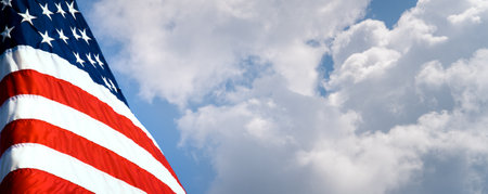 American flag waving in the wind against a blue sky with white cloudsの写真素材
