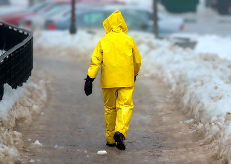 Man in a yellow protective suit and mask walks along a snowy road. Photographyの写真素材