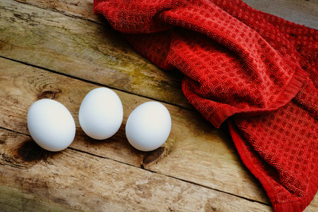 Three white eggs on a red napkin on a rustic wooden tableの写真素材