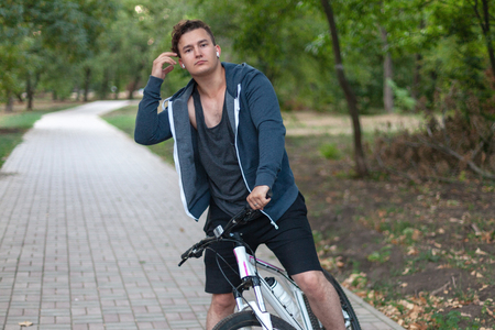Dark hair bicycling in the park Outdoors, autumn / fall park. Diversity people. Melancholy mood. Headphones (earphones, airpods), silver ring, white and rose bicycle.の写真素材
